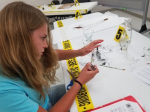student sitting at a table examining crime scene equipment.
