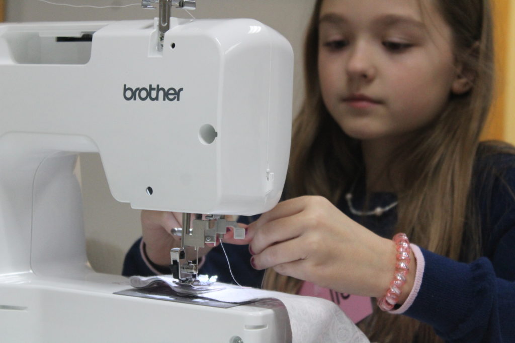 young girl sitting behind a sewing machine threading the needle.