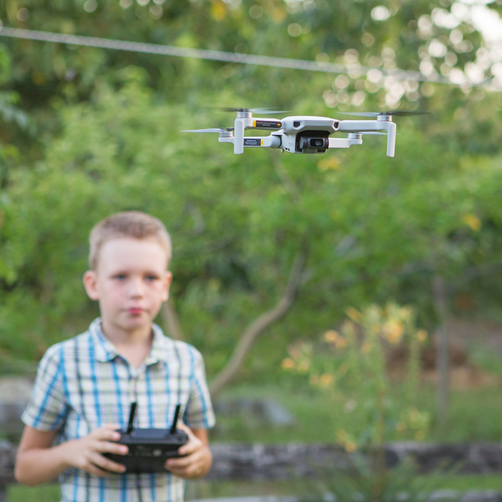 A boy in a checked shirt flies a drone around outside