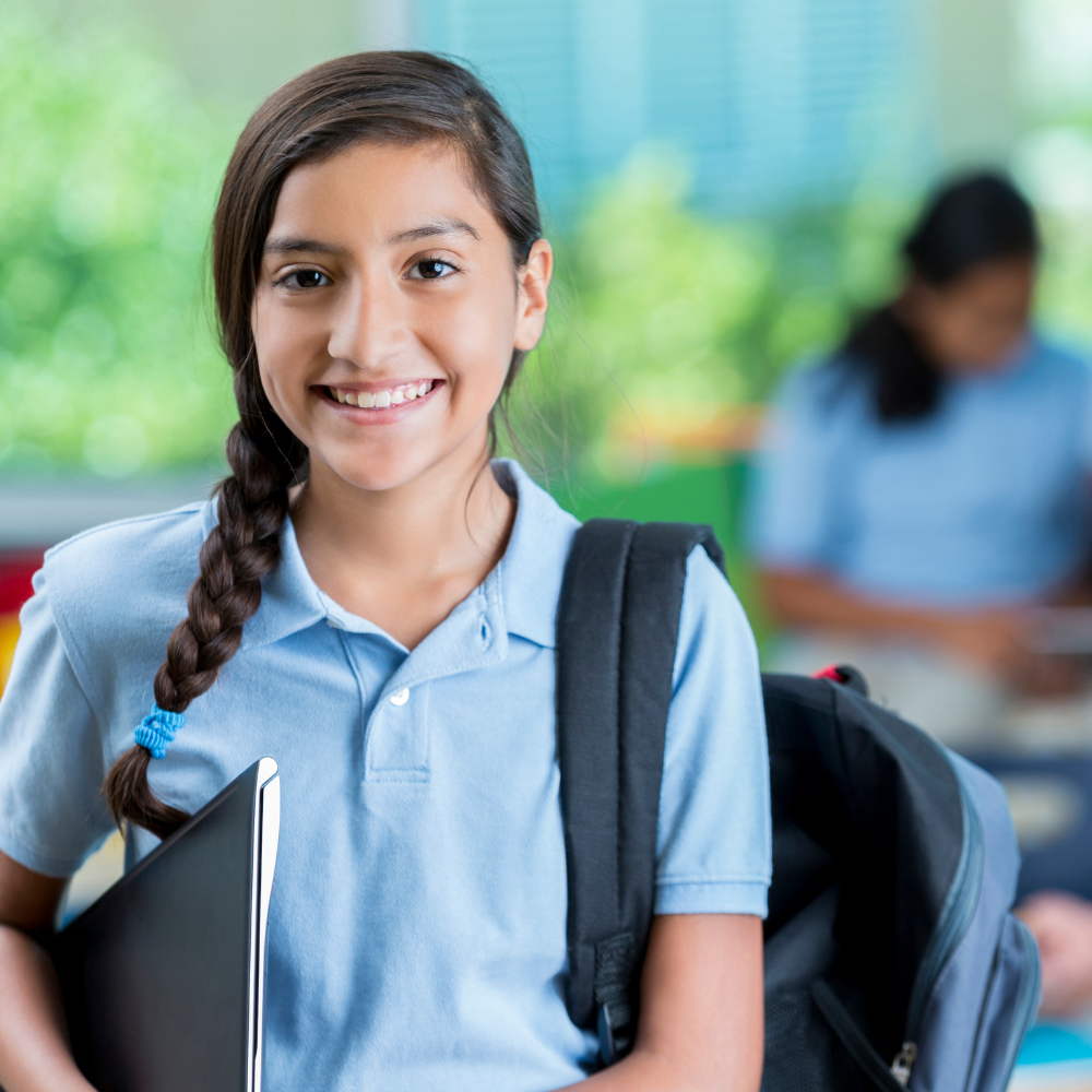 A girl with a braid smiling and holding a notebook and backpack