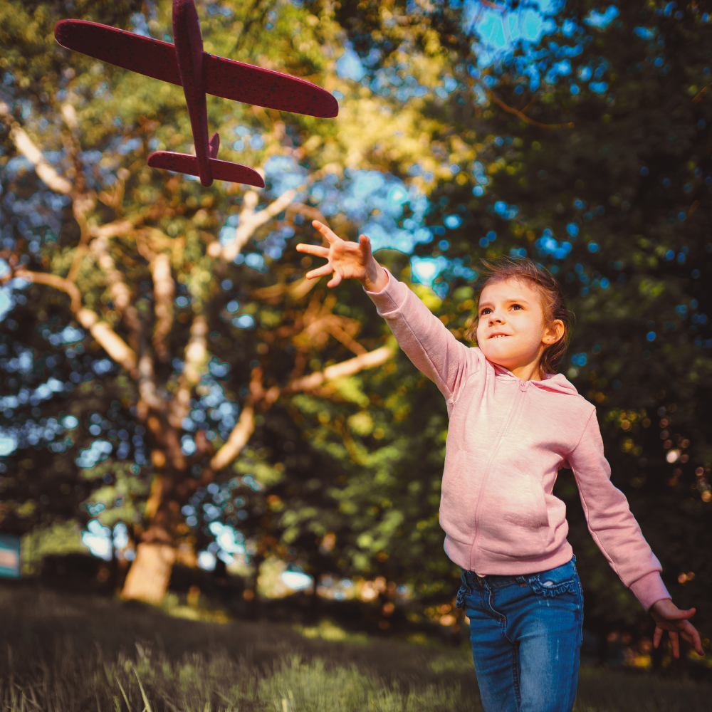 A girl in a pink sweatshirt throws a wooden plane