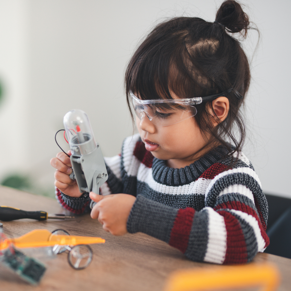 A young girl wearing safety goggles tests a small plastic light-up item