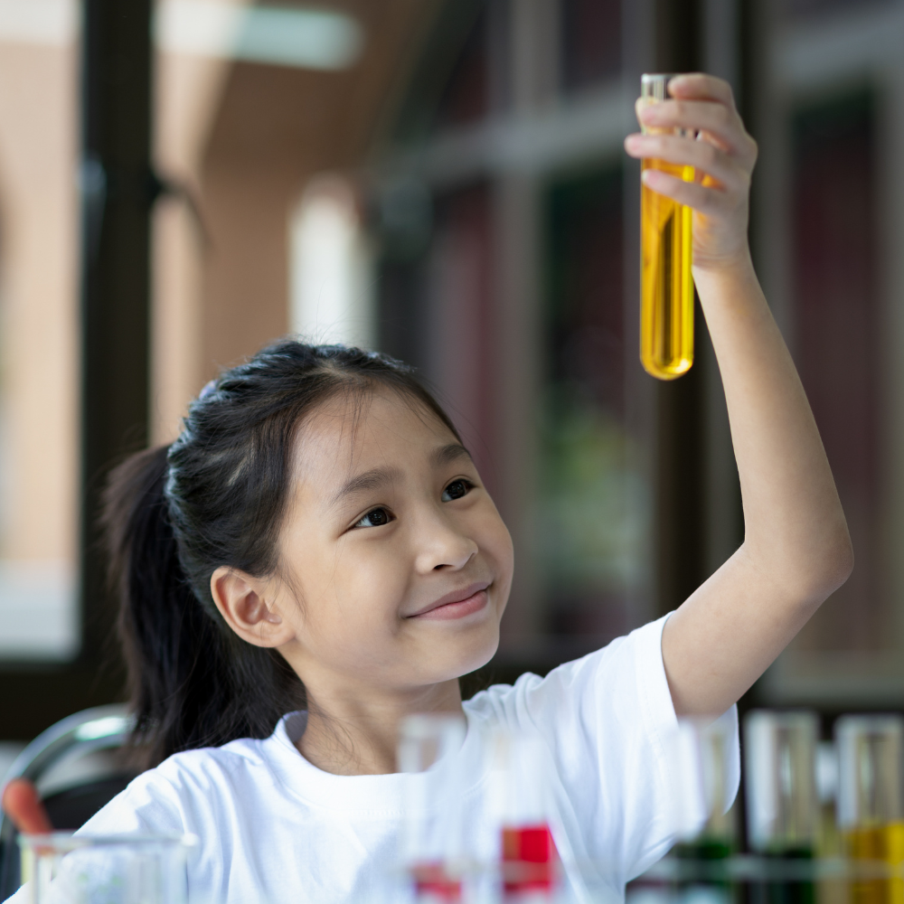 A young girl holds up a vial of orange liquid and studies it