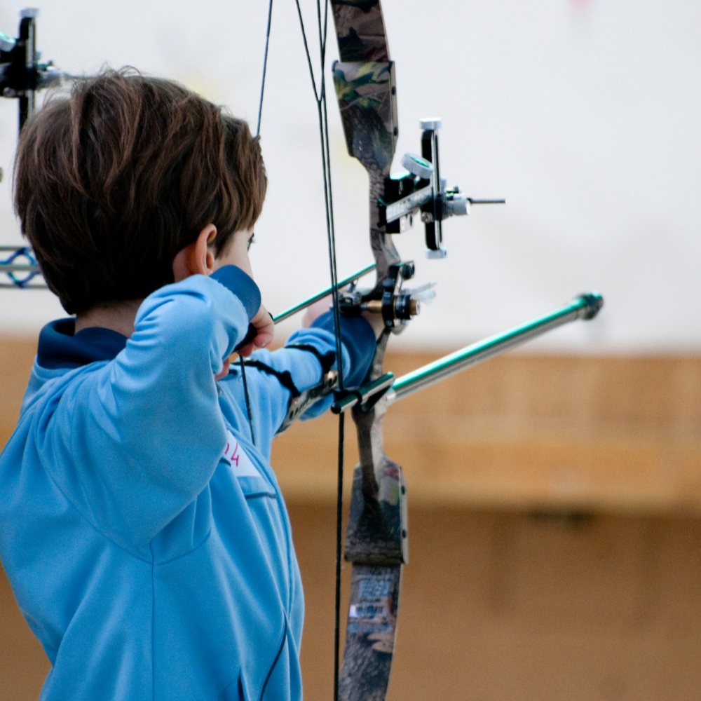 A young boy pulls back a bow with a green arrow