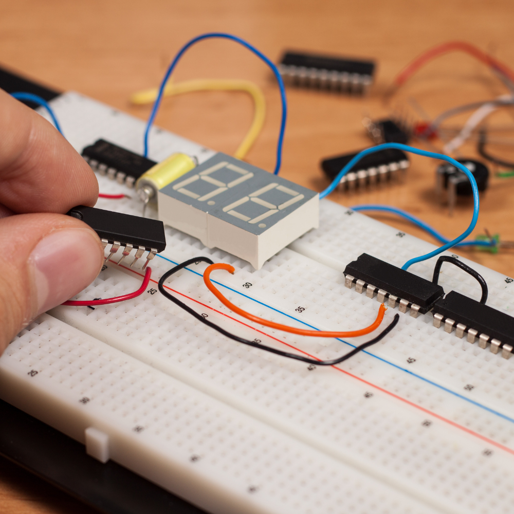 person plugging electric cords into a breadboard with a timer attached