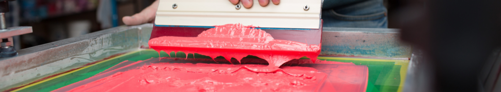 a person scrapes pink paint on a screen print sheet