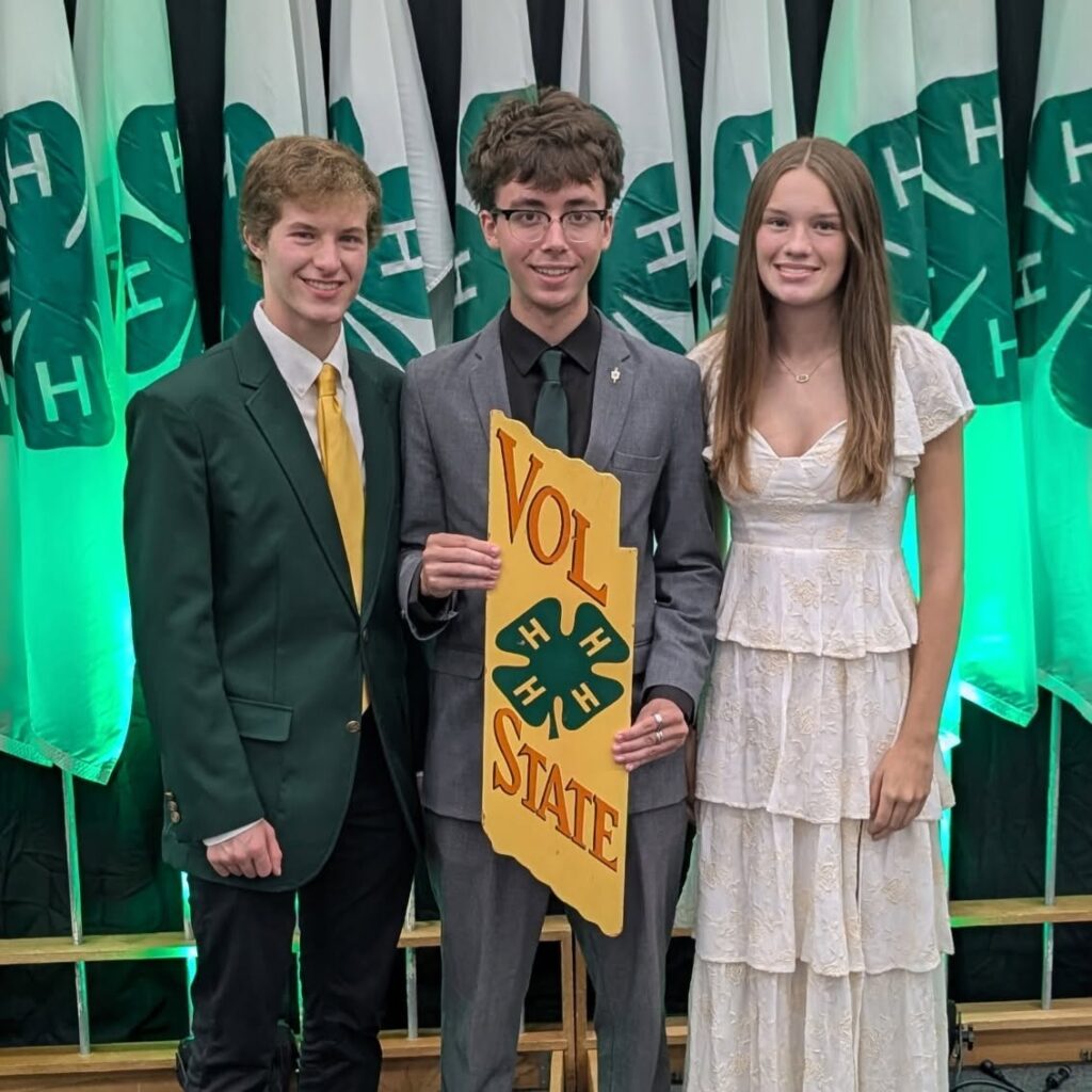 Matthew, Asa and Paili posing in front of 4-H flags with the Vol State board